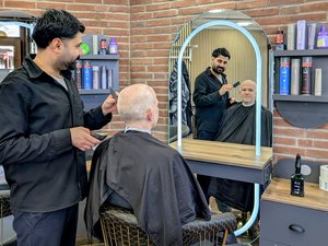 Geschäftsführer Sascha Lücke des Altenzentrums Bischof Stählin sitz im neu eröffnetem Friseursalon und wird von Friseurmeister Rasho Saadi frisiert. 