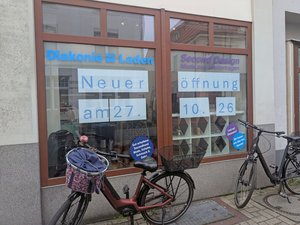 Schaufenster des Diakonie-Ladens Second Design in Nordenham mit Hinweisen auf die Neueröffnung am 27. Oktober 2026. Vor dem Geschäft stehen zwei Fahrräder.